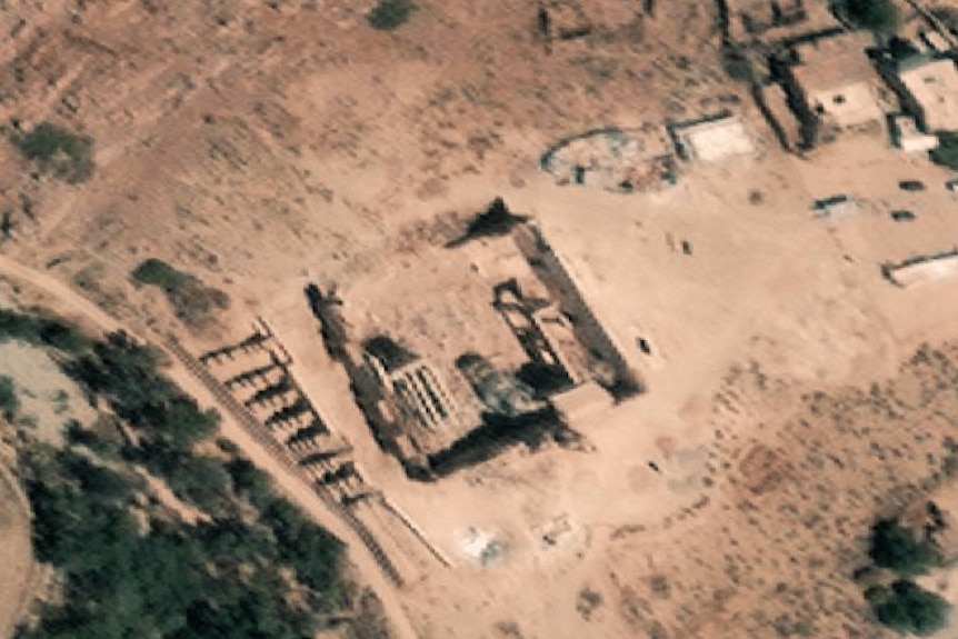A birds eye view shows the remains of a historic stone building in a dusty mountainous landscape. A wall is missing on one side