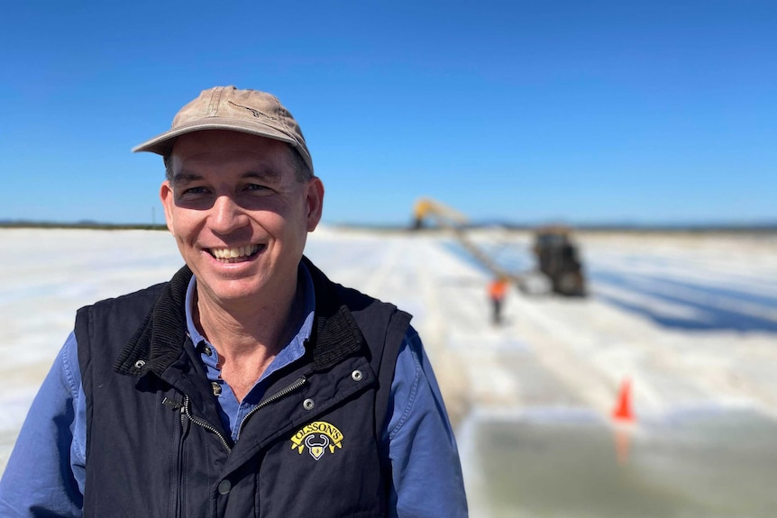 A man stands wearing a hat in front of a field of salt