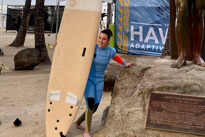 Person standing with surfboard next to a bronze statue 