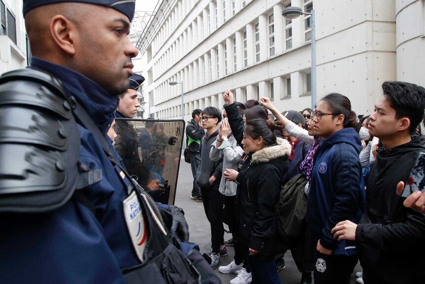 Demonstrators and riot police face each other outside a police station.