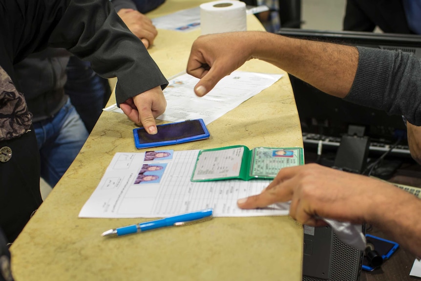 A man presses his thumb onto an ink pad as part of a passport application.
