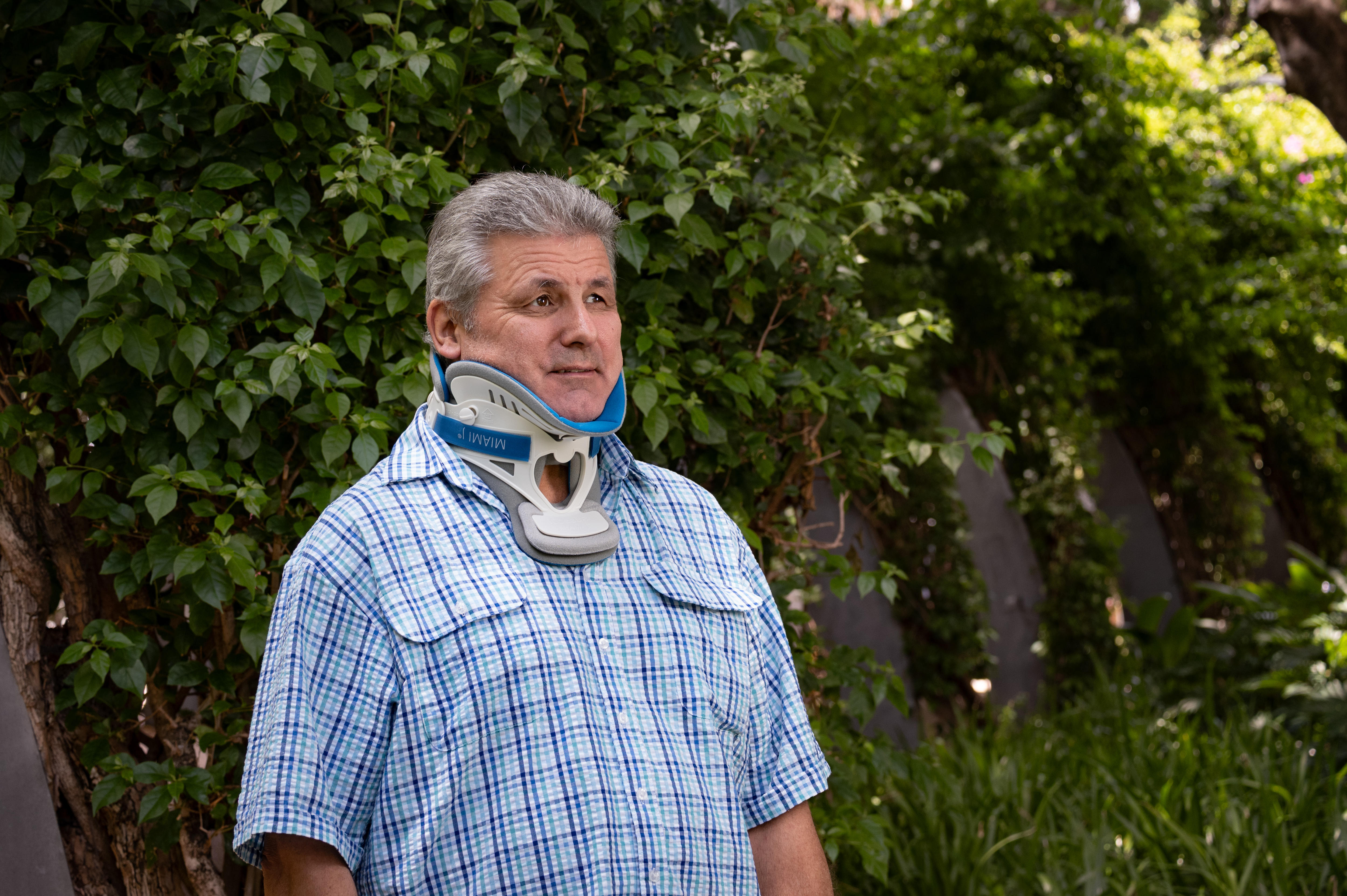 Un hombre con un collarín se para frente a un arbusto verde.