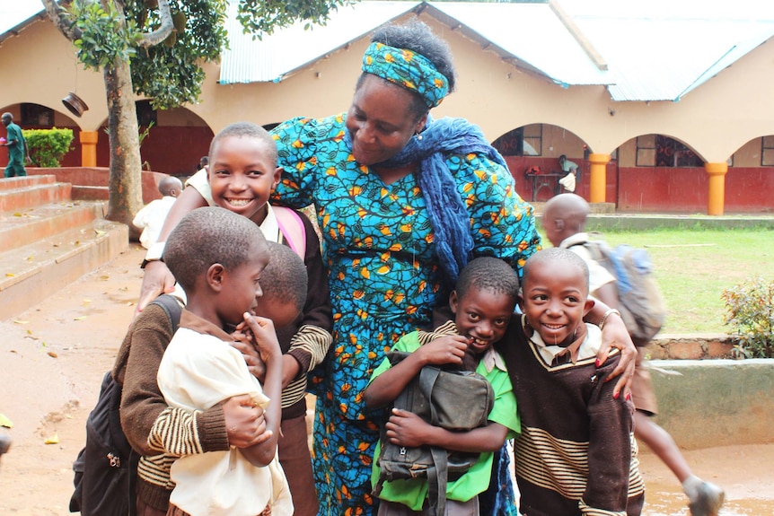 A woman stands with a group of smiling children.