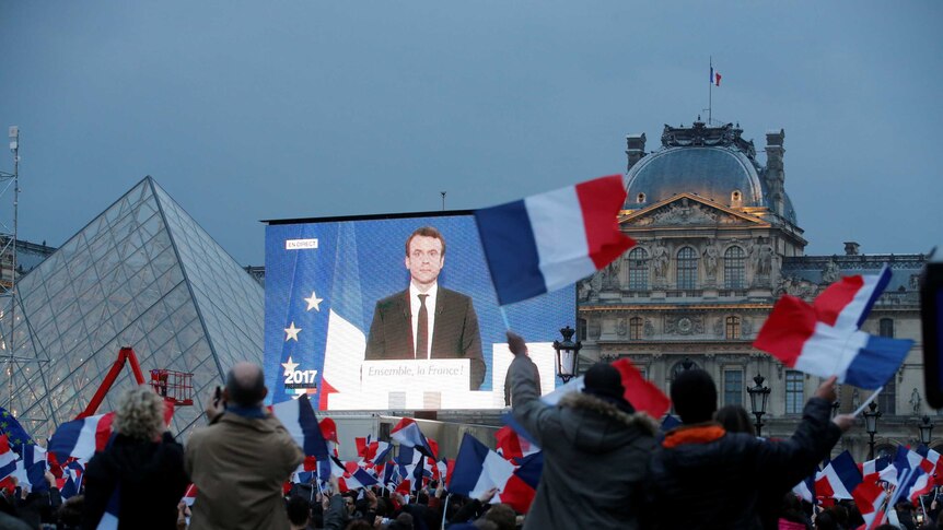 Macron speaks on a giant screen after results are announced.