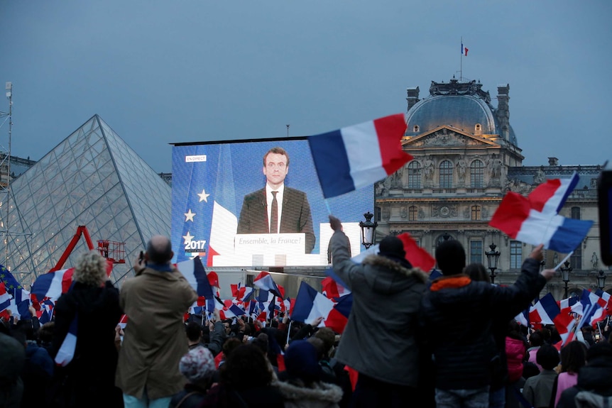 Macron speaks on a giant screen after results are announced.