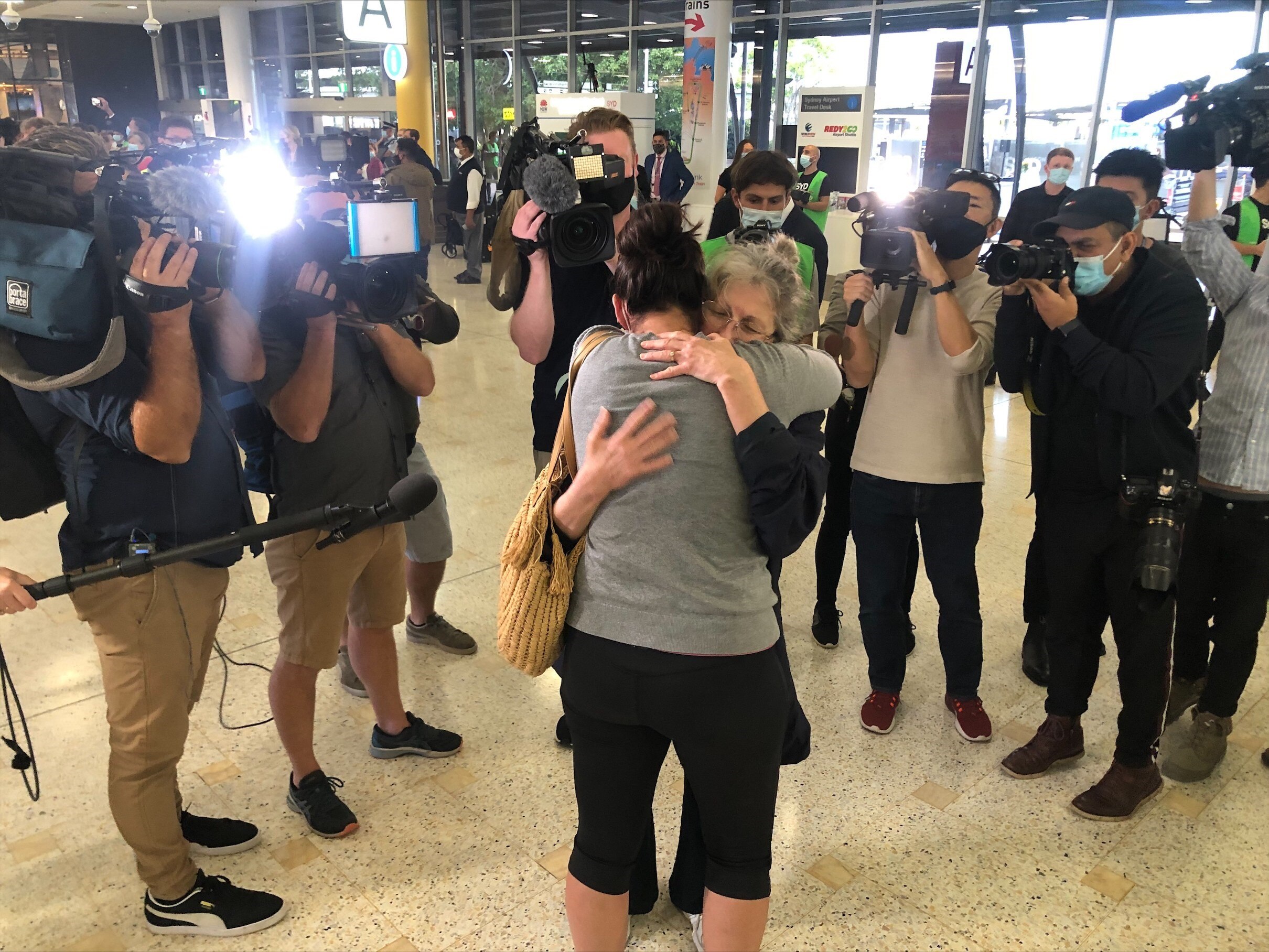 Two women hug while the media look on