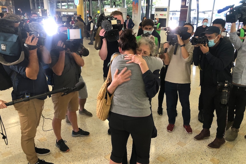 Two women hug while the media look on