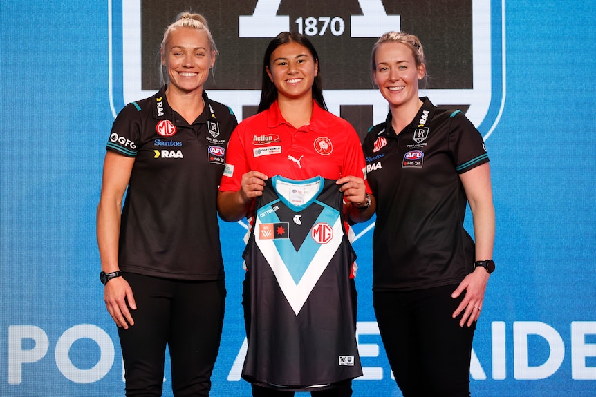Erin Phillips and Lauren Arnell stand either side of Hannah Ewings, who is holding a Port Adelaide guernsey at the AFLW draft.