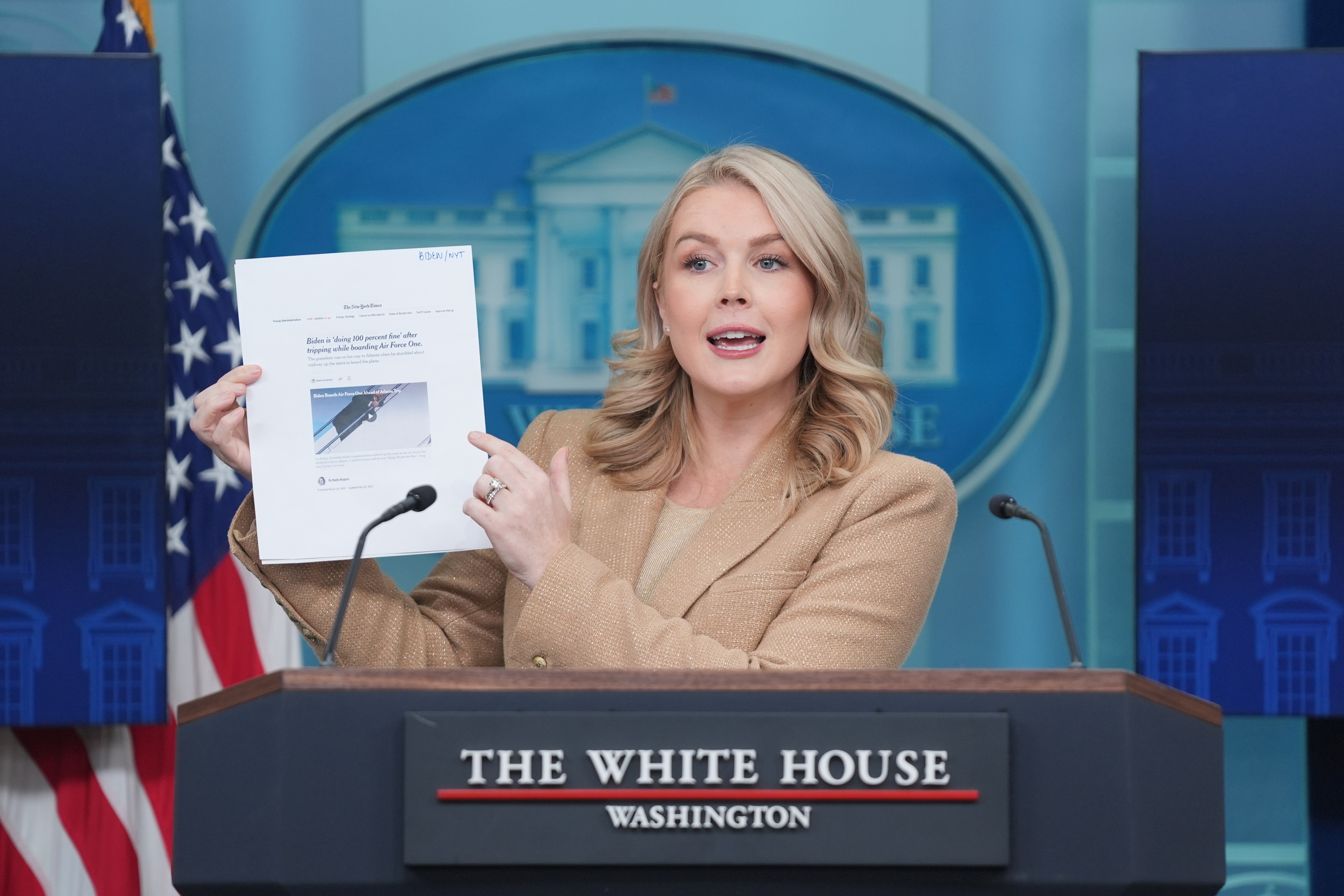 A professional looking woman holds up a printed article speaking a White House branded lectern. 
