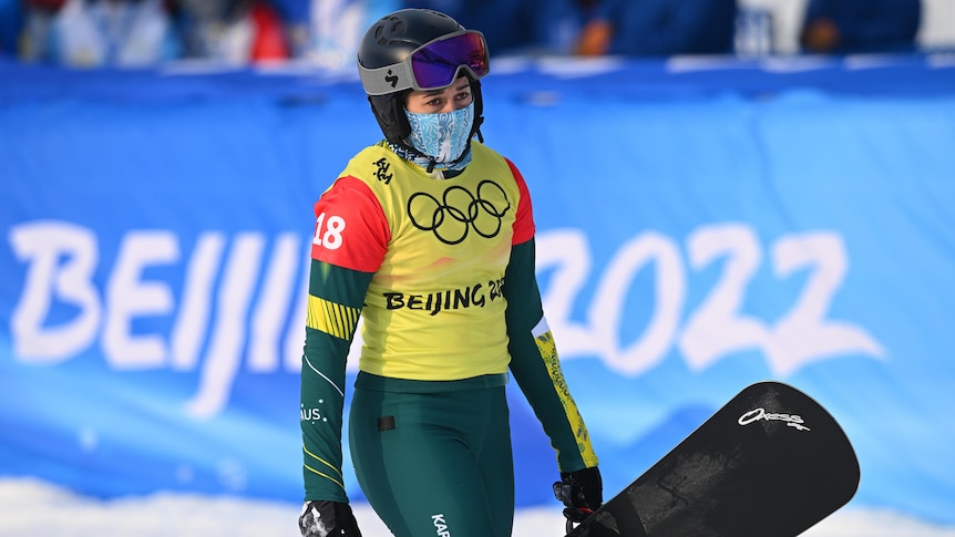 An Australian female snowboard cross competitor carries her snowboard at the 2022 Winter Olympics.