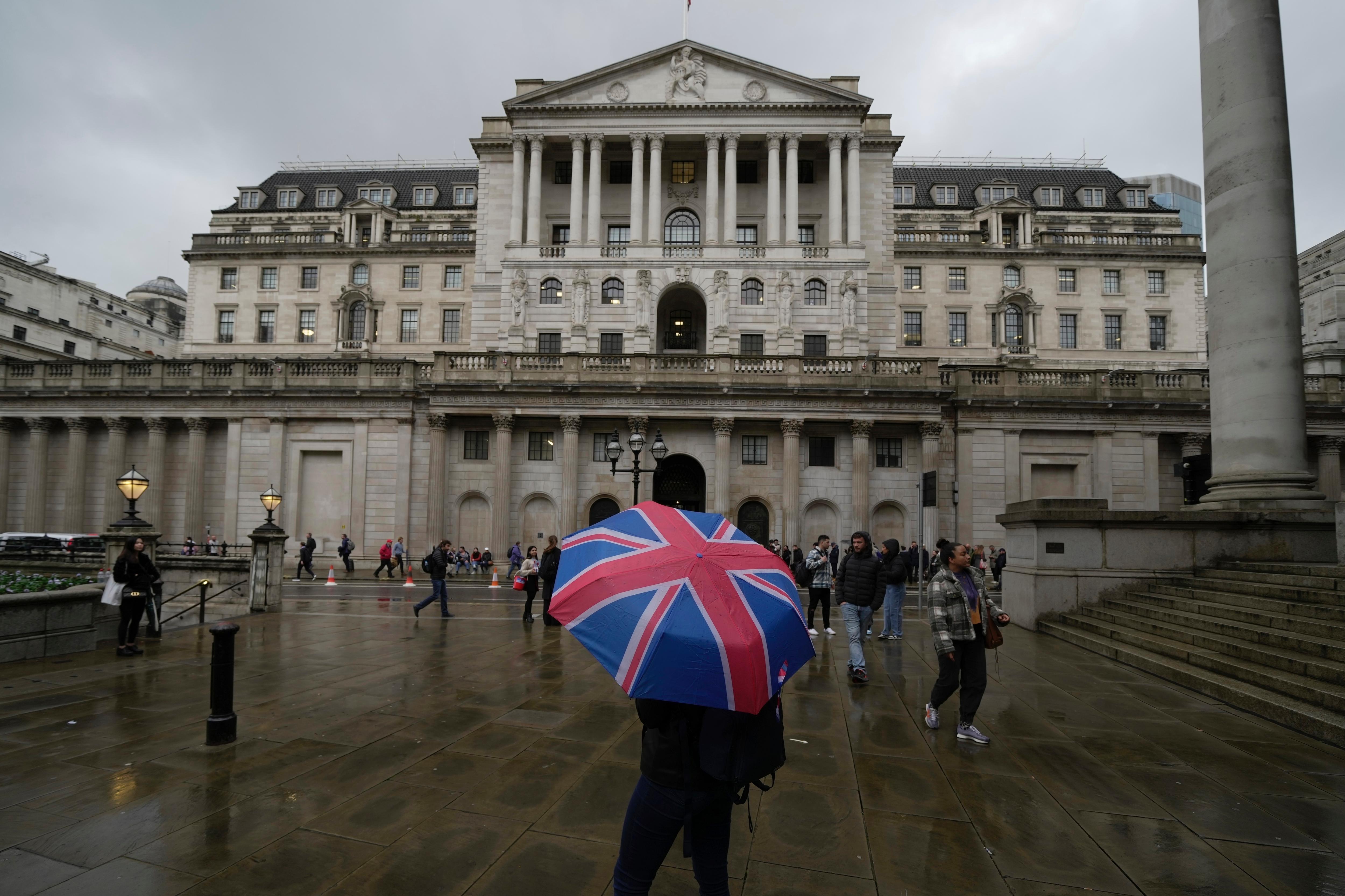 A person standing under a Union Jack umbrella in front of the white stone Bank of England building.