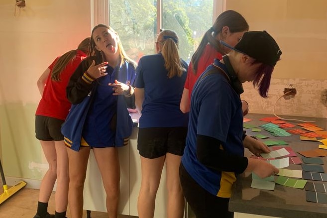 A group of young children stand in a room choosing paint colours