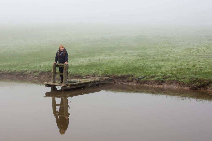 A woman stands alone in a wide shot of a misty field