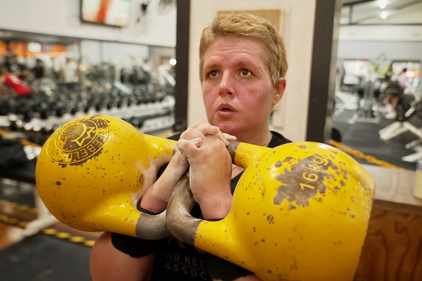 A woman holding two yellow kettlebells.