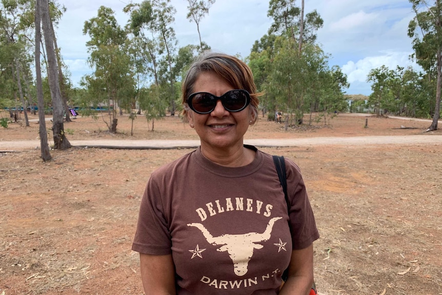 Ursula Raymond stands in a field wearing a brown shirt and sunglasses.