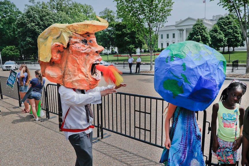Demonstrators wearing paper mache heads representing President Donald Trump and the planet Earth walk by the White House.