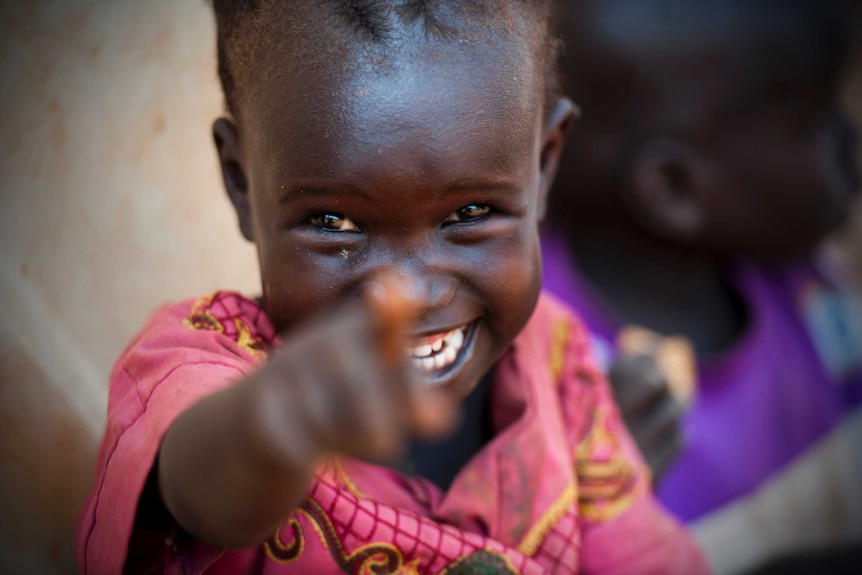 A girl in a refugee camp in war devastated Sudan points and smiles at a camera