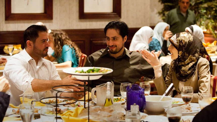 Two men and one woman in hijab eat dinner