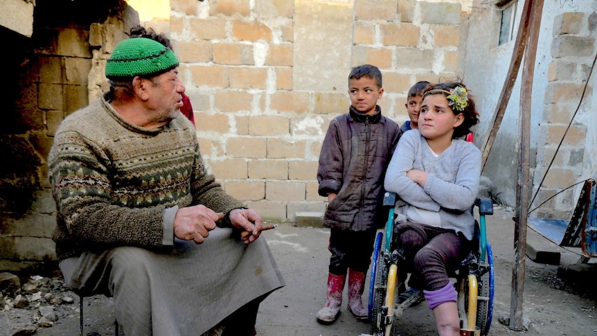 A girl in a wheelchair sits with her father and brothers in a courtyard