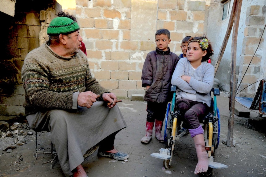 A girl in a wheelchair sits with her father and brothers in a courtyard