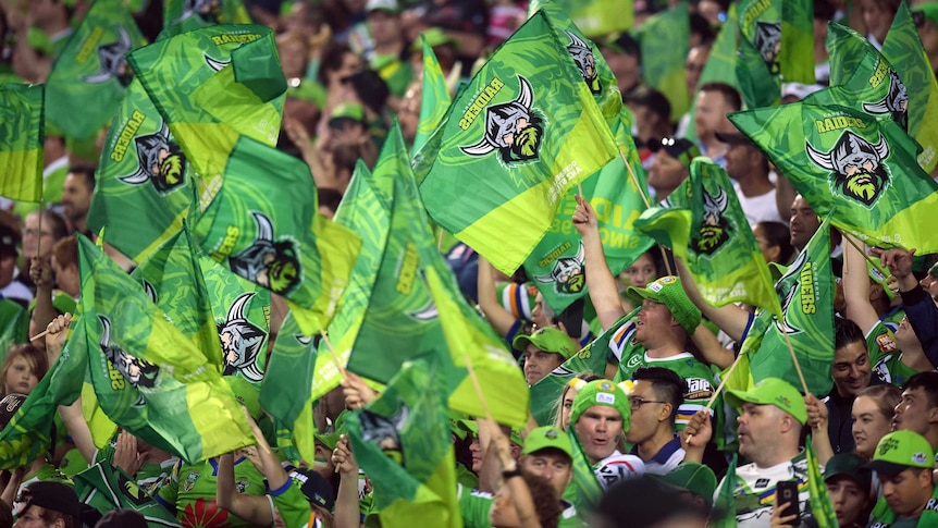 A section of the crowd at the NRL grand final stand waving their Canberra Raiders flags and banners.