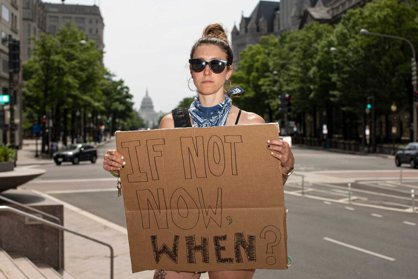 A white woman in DC holding a sign reading 'if not now, when?'