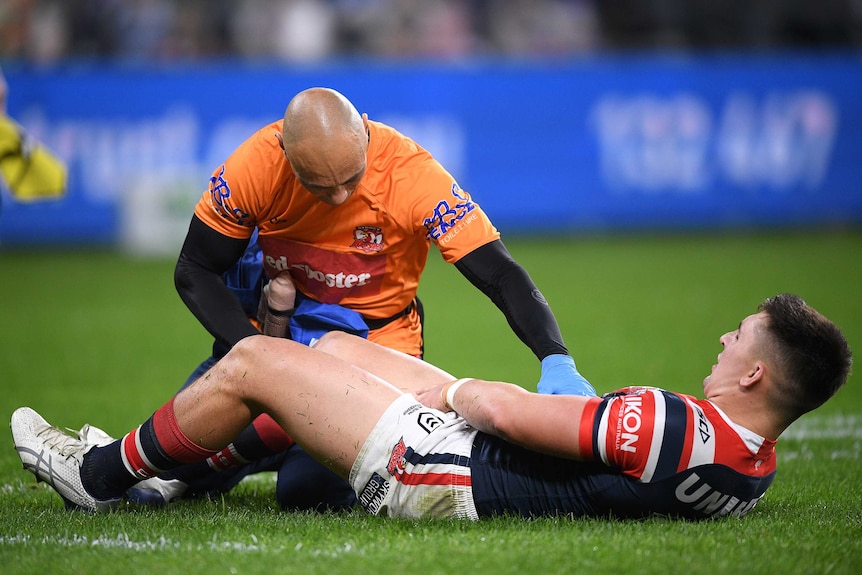 A Sydney Roosters NRL player lies on the ground as he receives treatment on a knee injury against St George Illawarra.