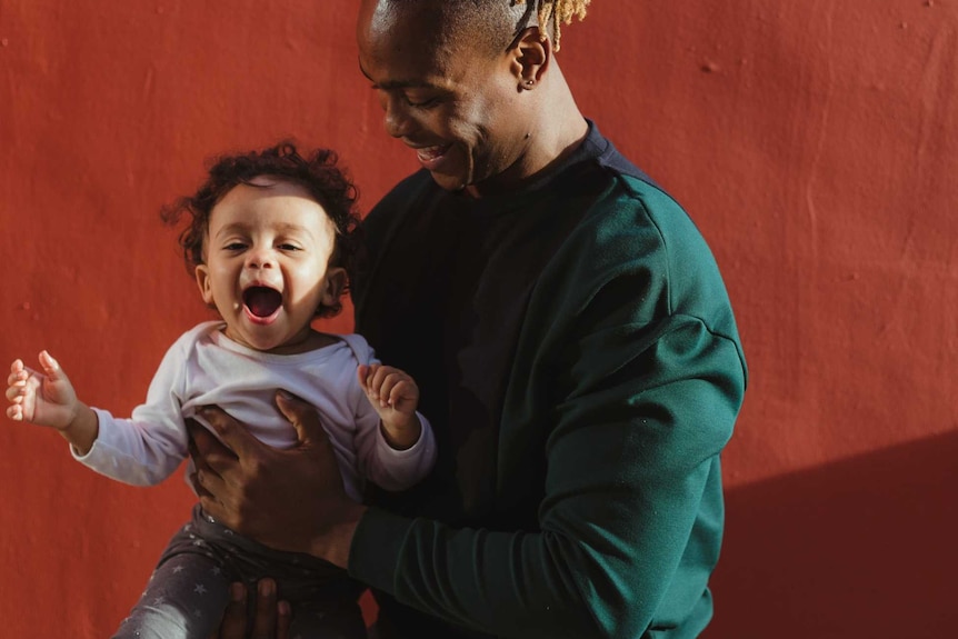 A man with dark skin holding a happy, smiling toddler
