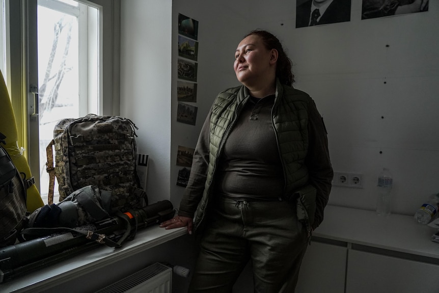 A woman in combat gear looks out a window 