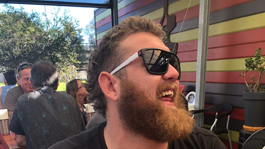 Jake laughs while sitting at a table in what looks like the outdoor area of a pub or restaurant.