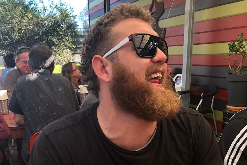 Jake laughs while sitting at a table in what looks like the outdoor area of a pub or restaurant.