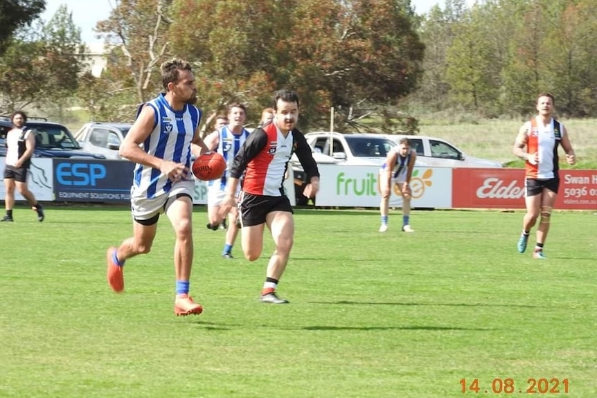 Footballer holds footy while running away from opponent