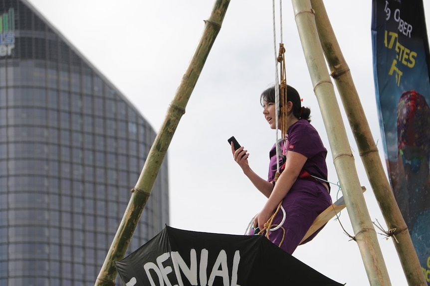 Close up of protester holding mobile phone while suspended over bridge.