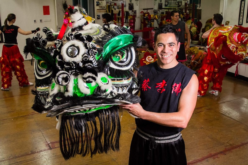A man holding a black, green and white lion dance costume head.