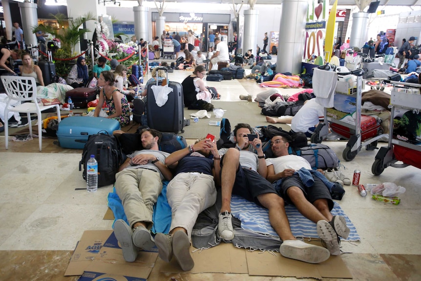 People lying on makeshift mats on the ground inside an airport.