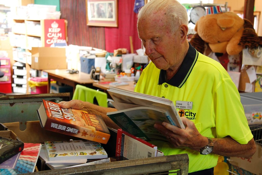 An elderly man in a high-vis polo shirt sorting donated books.