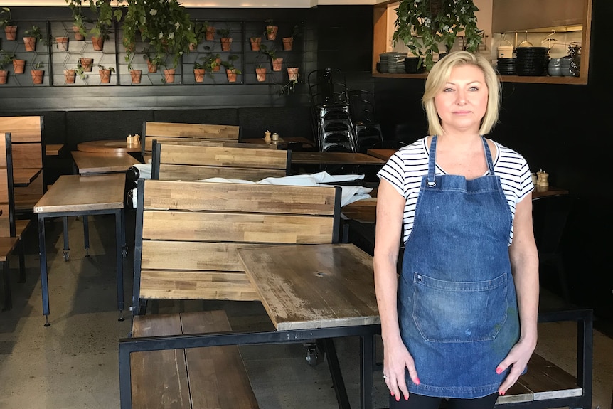 A woman wearing an apron stands inside a cafe.