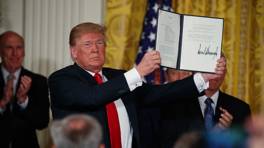 President Donald Trump holds up signed document