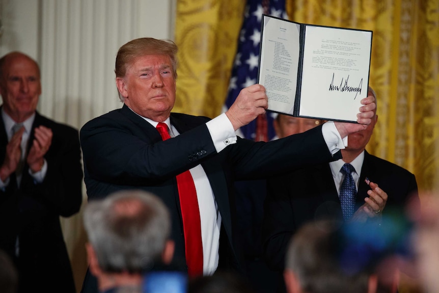 President Donald Trump holds up signed document