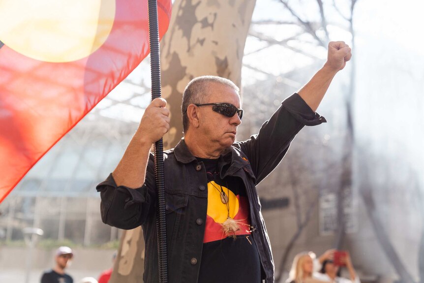 A protestor holds out an Aboriginal flag and his fist in the air in the "Black Power" signal.