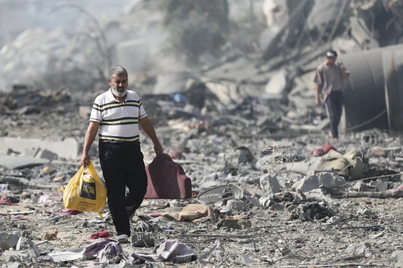 A man carrying a plastic shopping bag walks across rubble and destroyed buildings