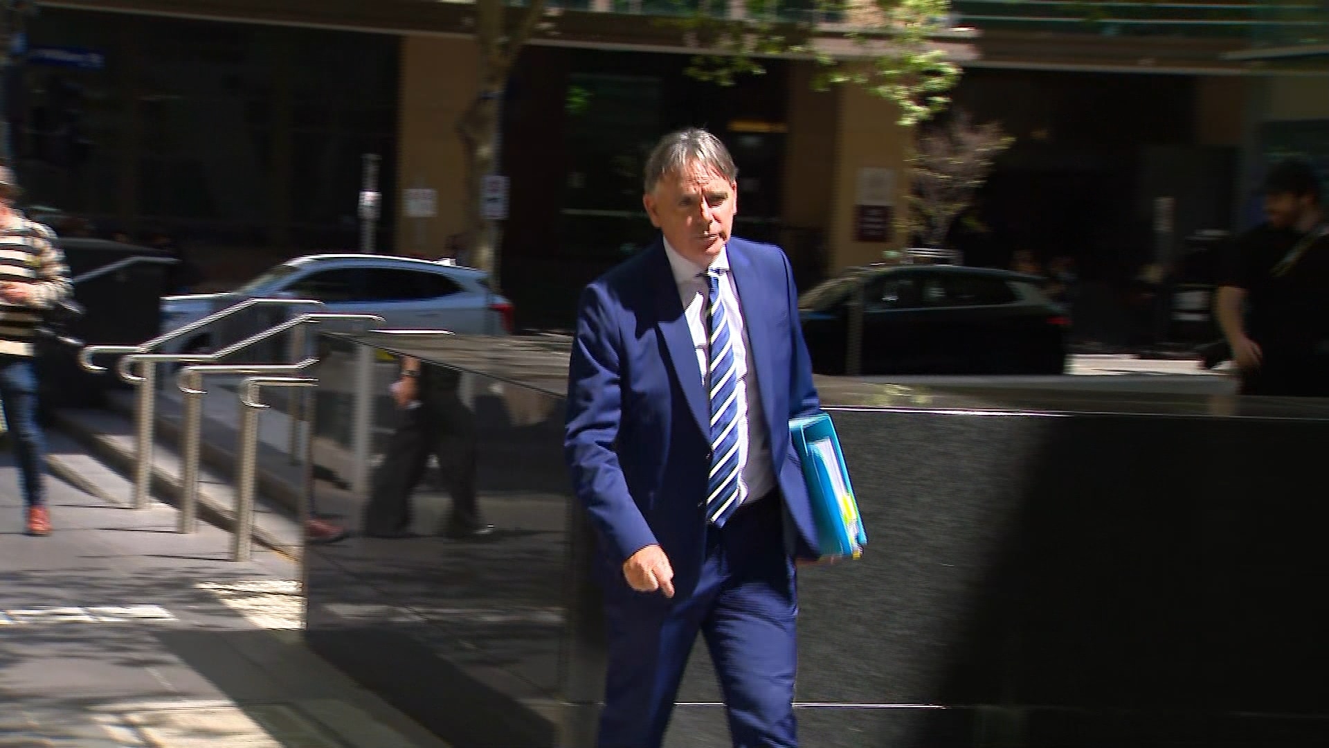 Dermot Dann wears a suit while walking along a footpath.