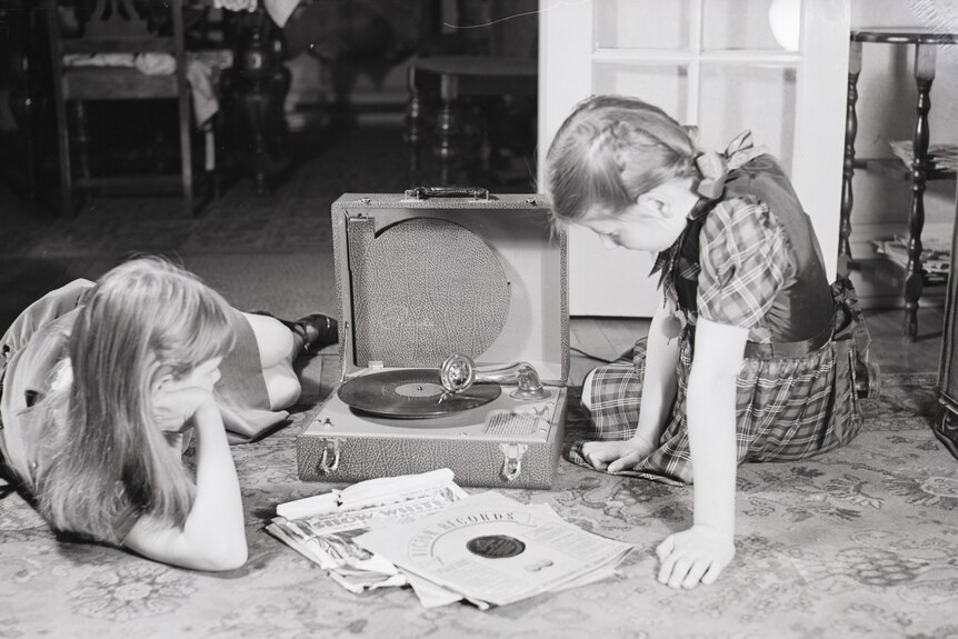 A black and white photo of two young girls near a phonograph with a small pile of audio discs between them.