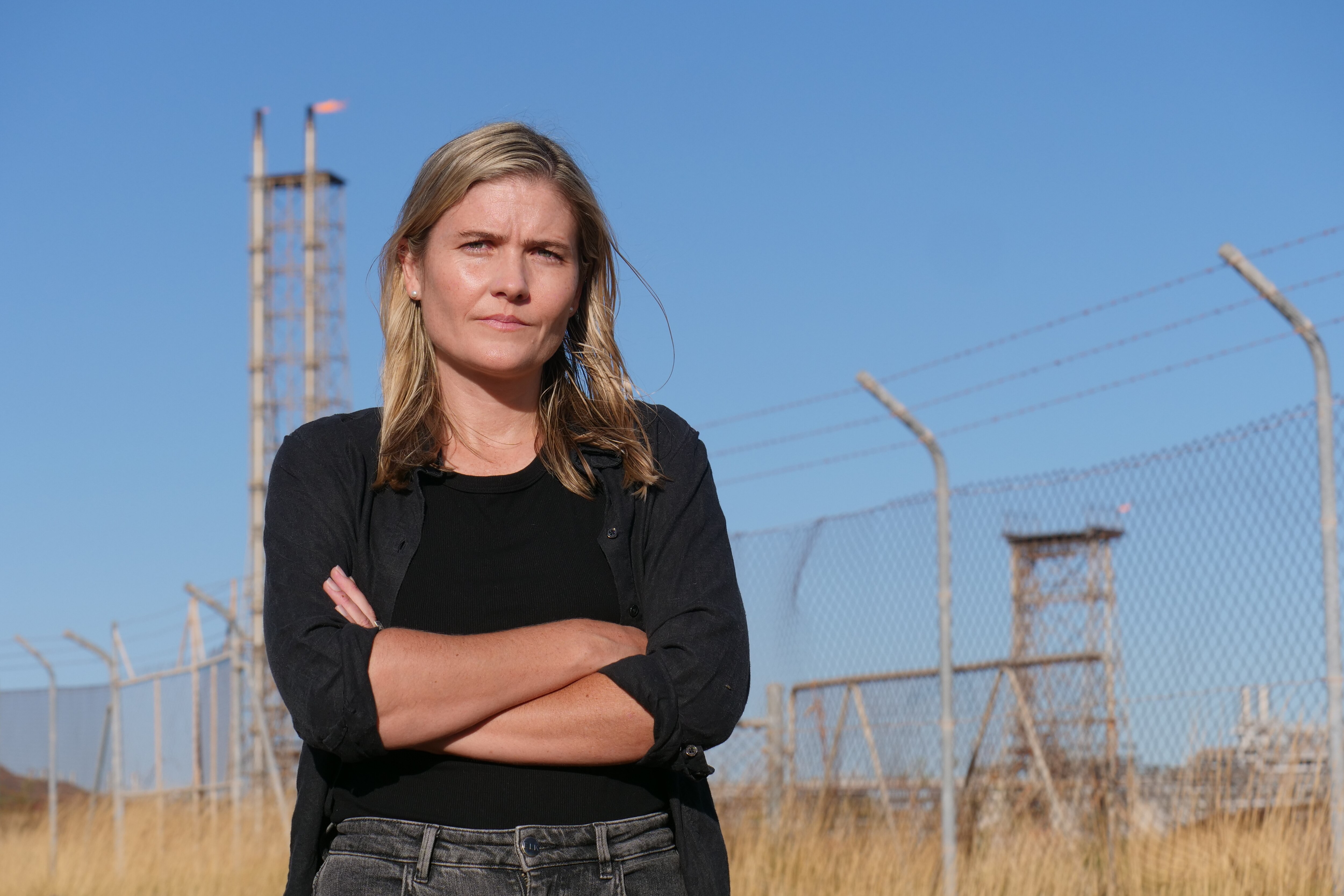 Mulher vestindo uma camisa preta e jeans em pé perto de uma cerca.