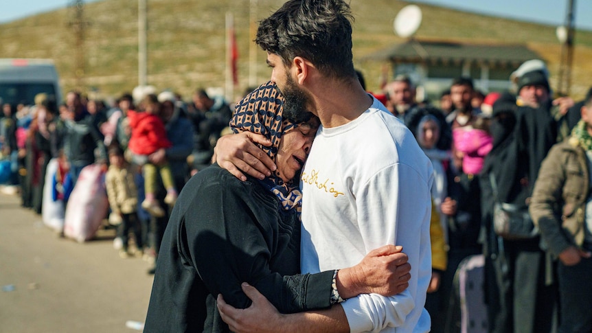 A man kisses the forehead of a grieving mother while surounded by crowds of people.
