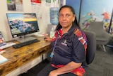 A woman sitting at a desk in an Indigenous jersey