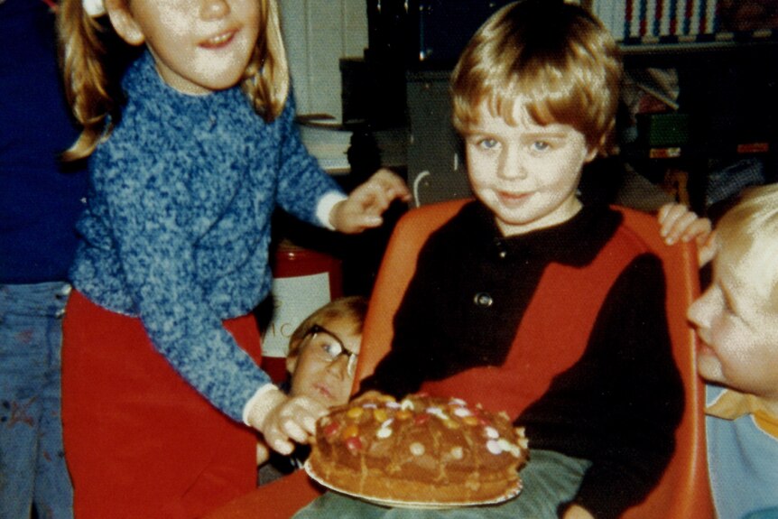 A little girl hands a little boy a birthday cake.
