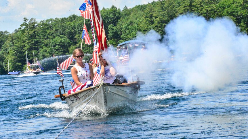 Smoke comes out of a cannon on a boat covered in US flags.