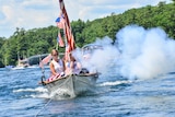 Smoke comes out of a cannon on a boat covered in US flags.
