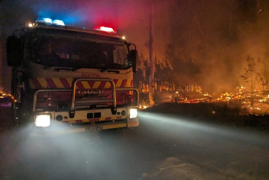 Fire truck with fire burning in background at night